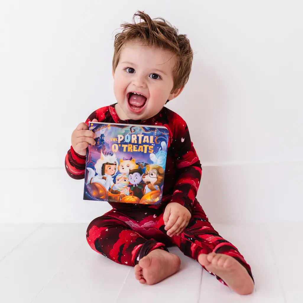Child wearing red and black pajamas holding a 'Portal of Treats' book on a white background