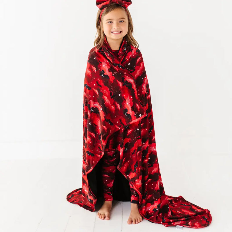 Child wrapped in a red and black patterned blanket on a white background