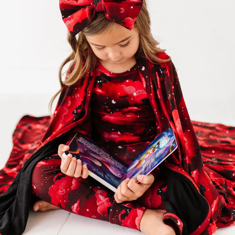 Child in a red and black outfit with a large bow, holding a colorful book.