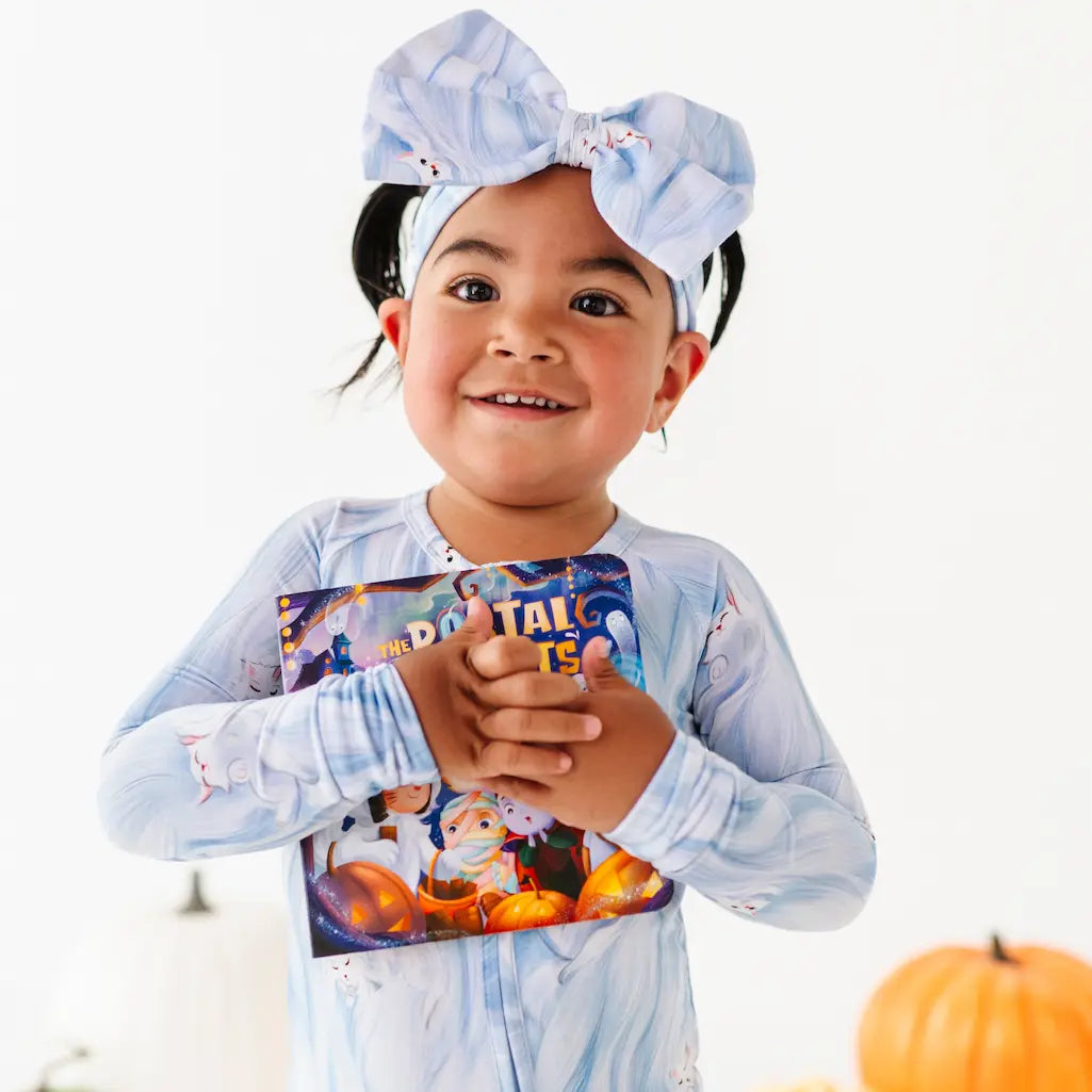 Child wearing a blue outfit with a bow, holding a book, on a white background