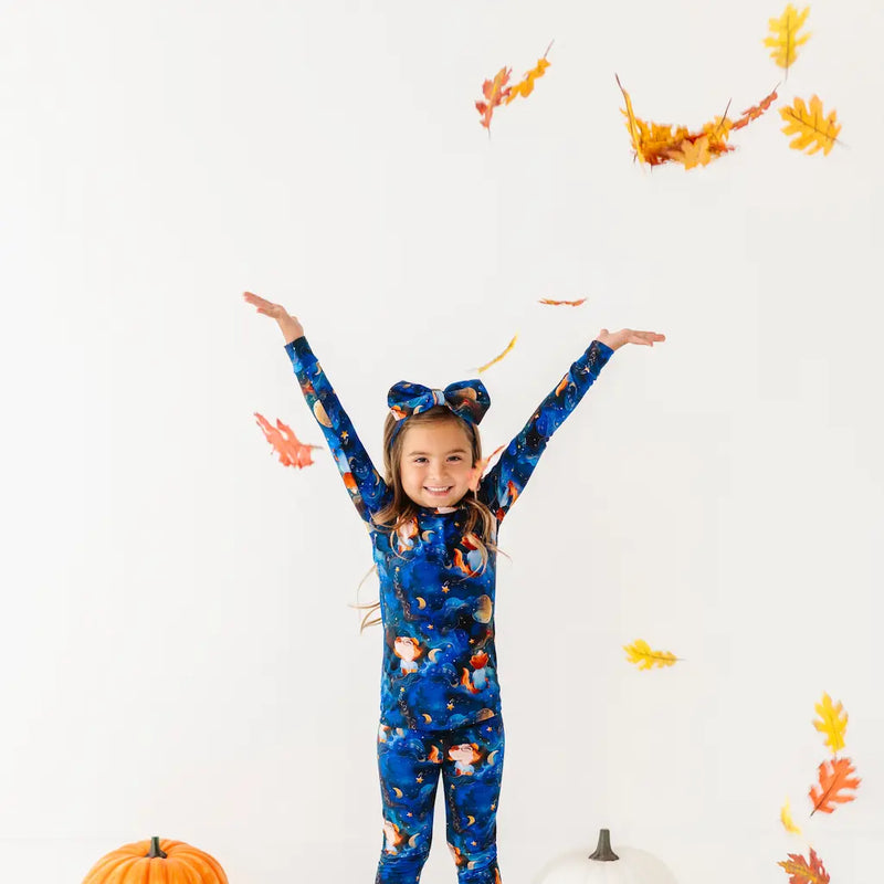 Child wearing a blue onesie with animal prints, surrounded by autumn leaves and pumpkins on a white background.
