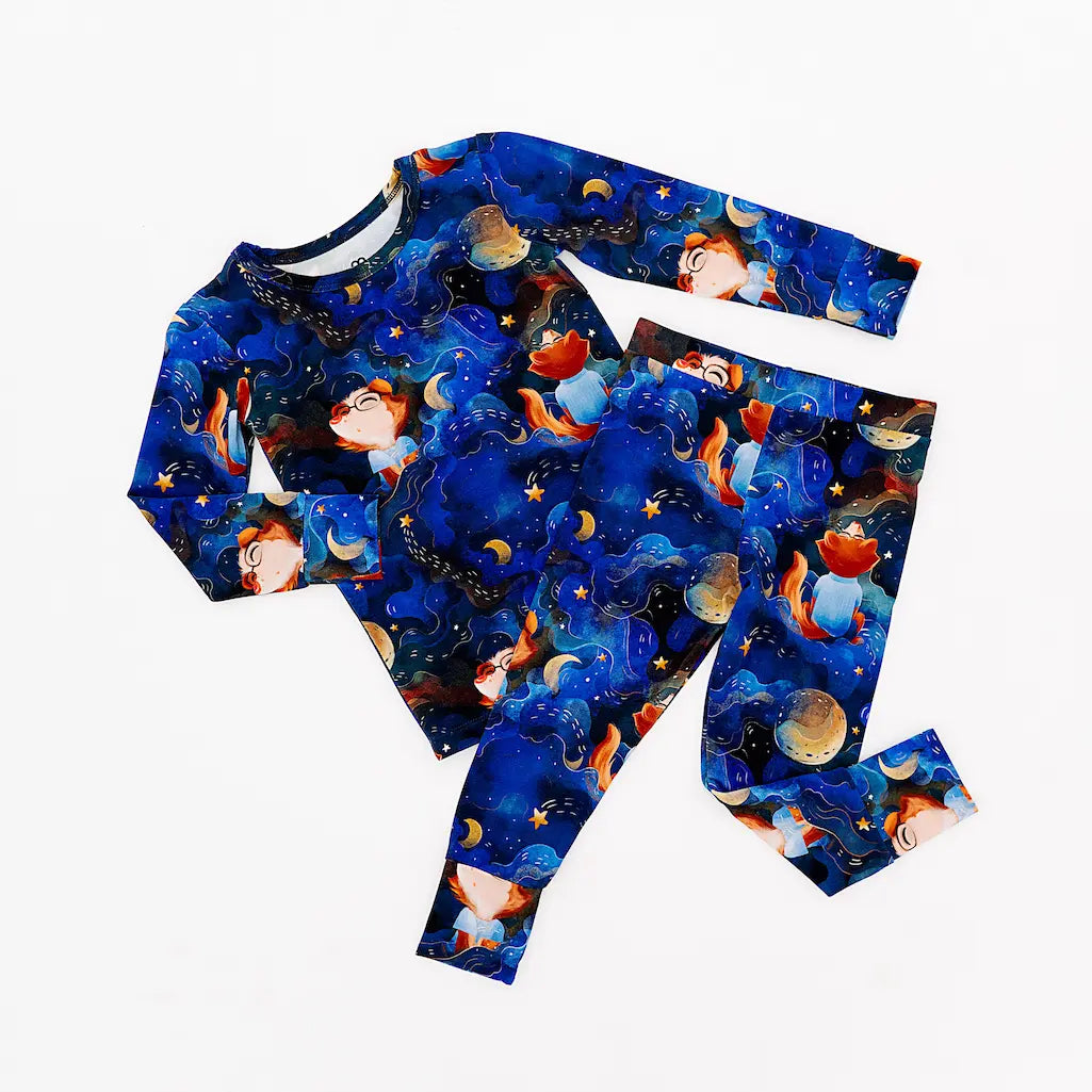Dark blue pajama set with colorful space-themed illustrations including planets, stars, and astronaut characters, laid flat on a white background
