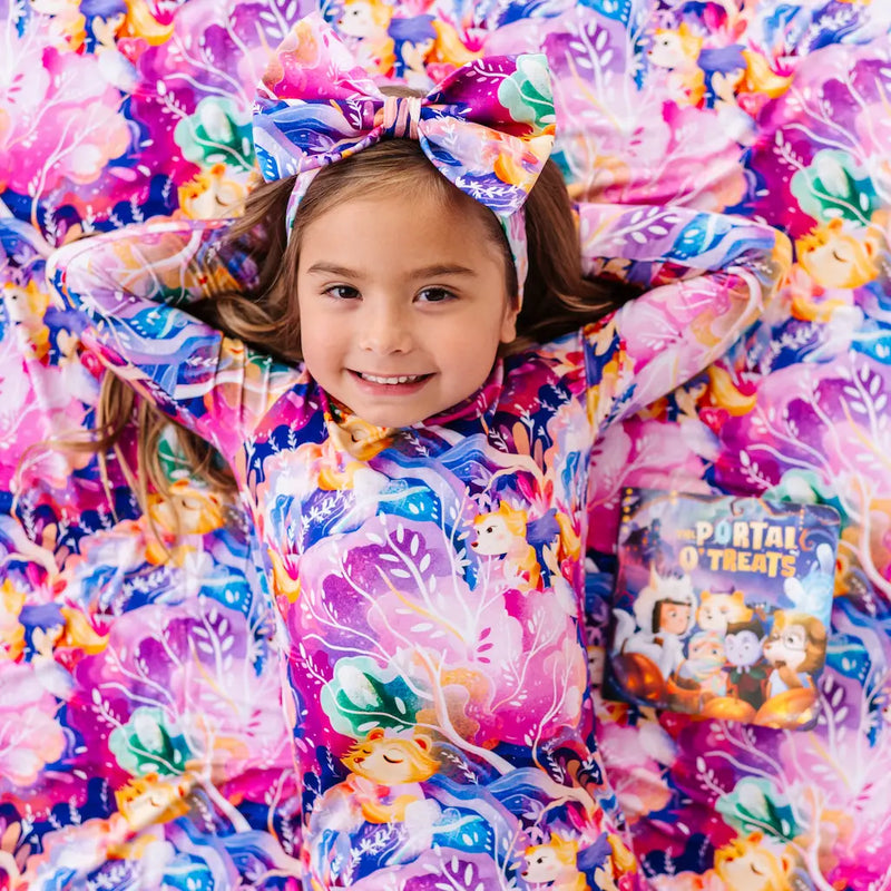 Child wearing a colorful outfit with a large bow, surrounded by similar patterned fabric.