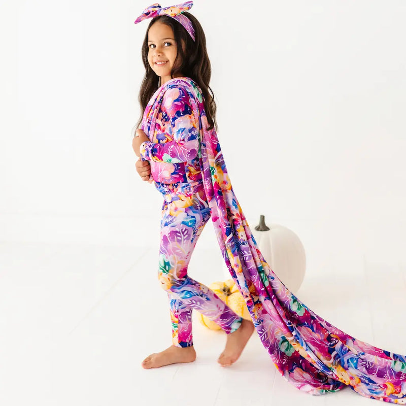 Young girl wearing a colorful floral onesie with a matching scarf on a white background