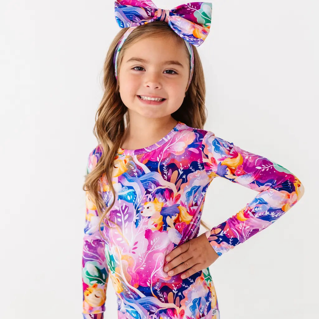 Young girl wearing a colorful long-sleeve shirt with a floral pattern and a matching headband on a white background.