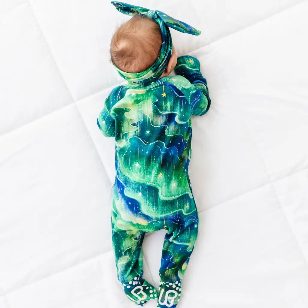 Baby wearing a green and blue galaxy-themed onesie on a white blanket