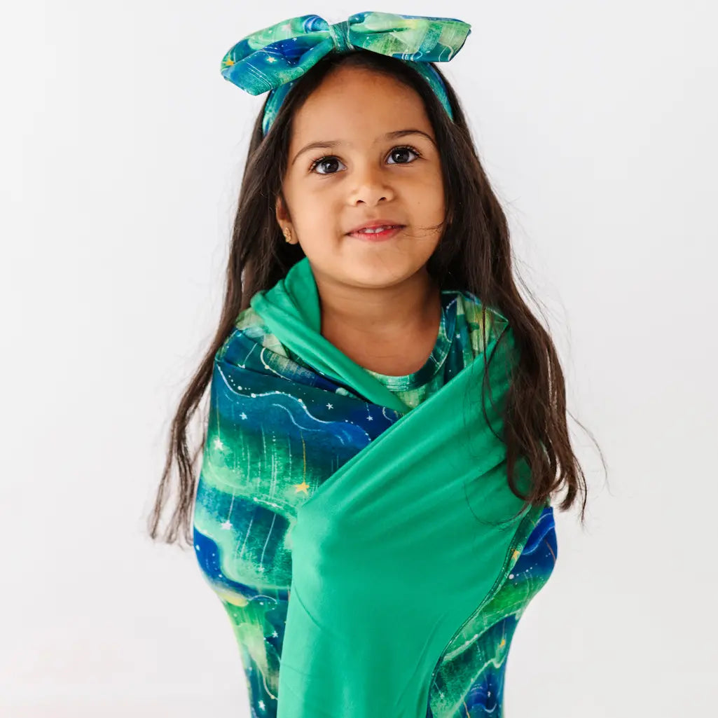 Young girl wearing a green and blue patterned headscarf and dress on a white background
