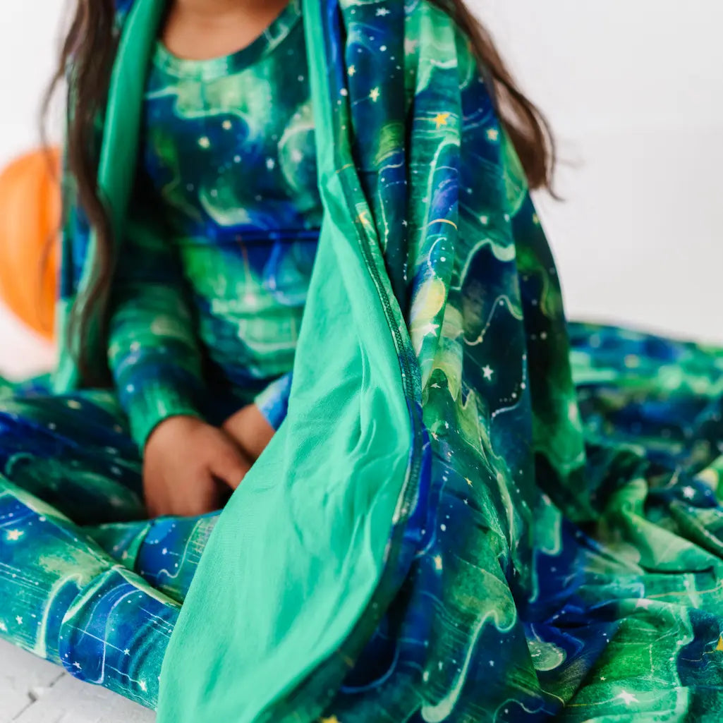 Child wearing a green and blue space-themed outfit with a matching blanket.