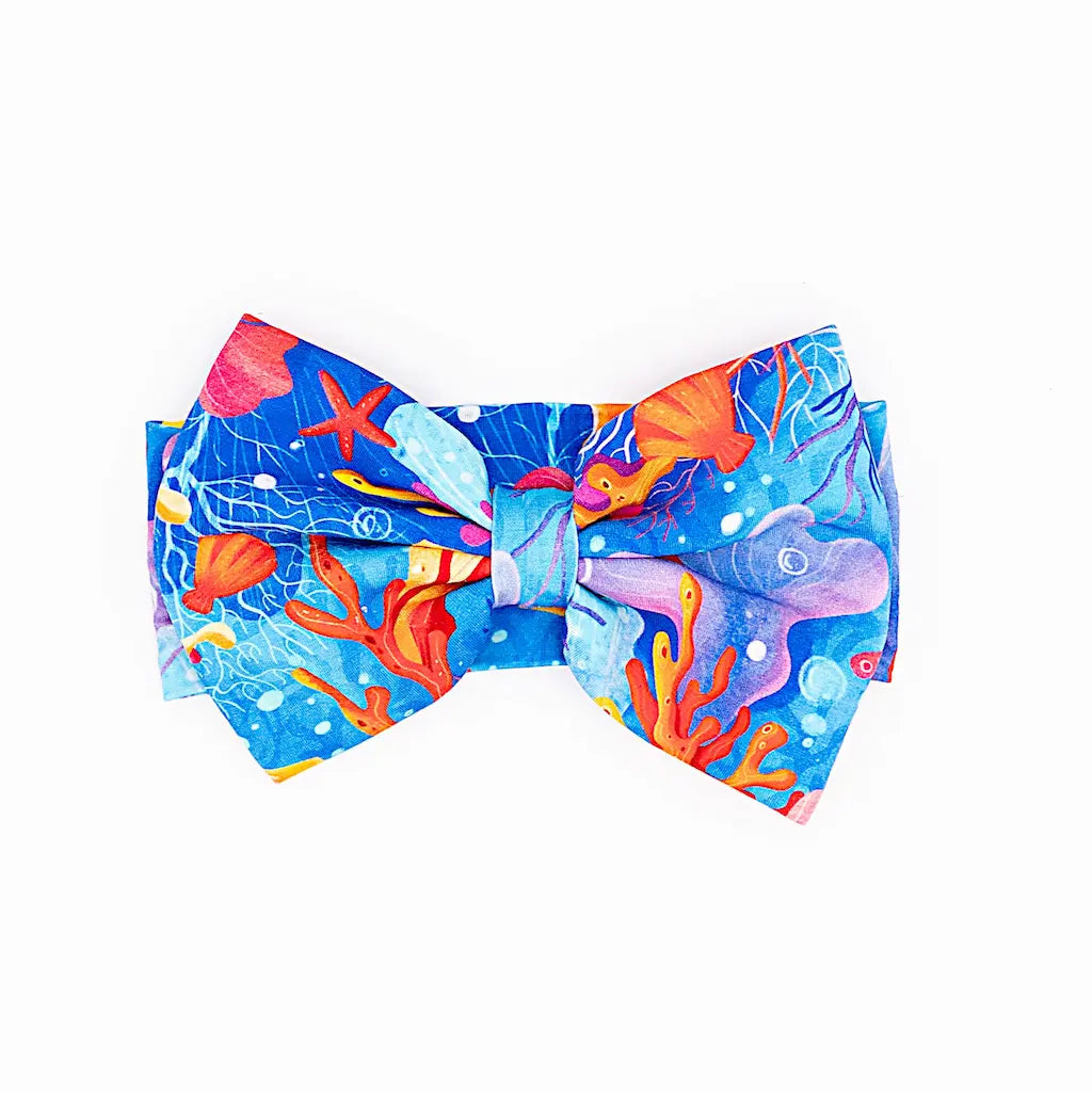 A bow-shaped headband with a printed pattern resembling a mystical reef with corals and sea plants in blue, orange, and purple colors.