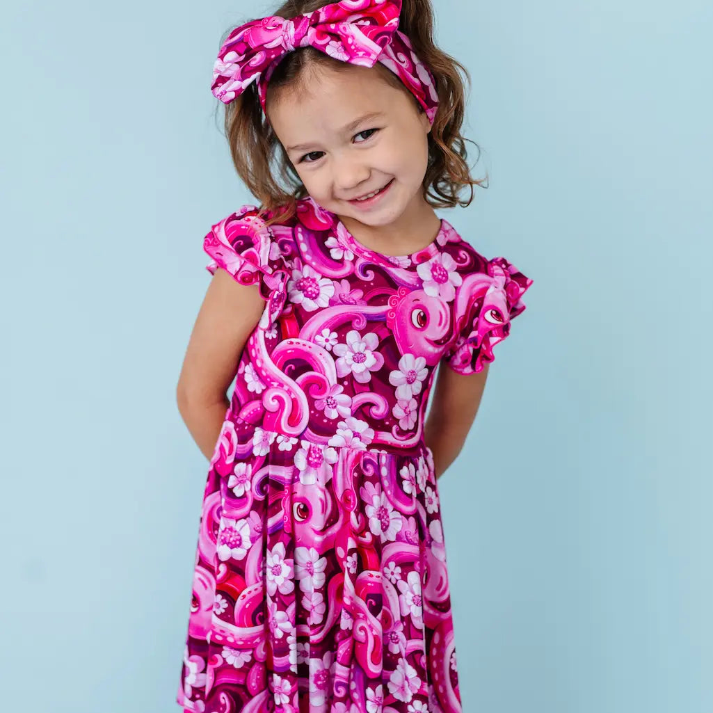 Young girl wearing a pink floral dress and headband against a light blue background