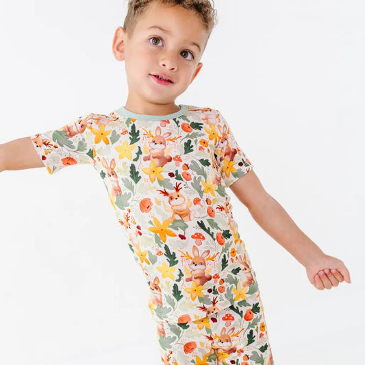 A child with an arm outstretched wearing a short sleeve pajama top with sage trim in a woodland jackalope print.