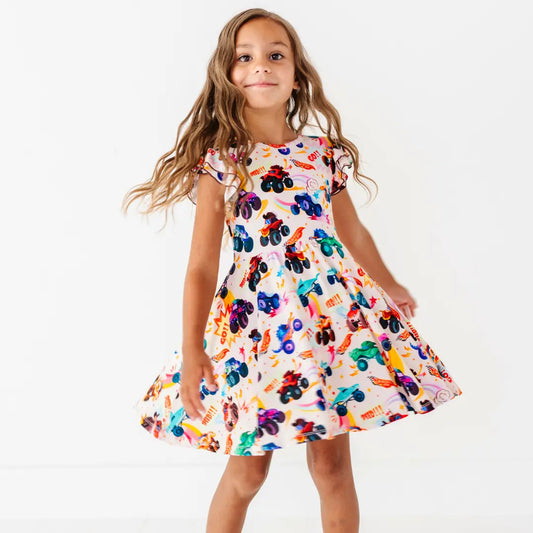A child twirling in a cream flutter-sleeve dress with a colorful monster truck print.