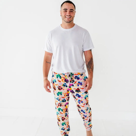 A father smiling in a white tee and men's pajama pants with a colorful monster truck print.
