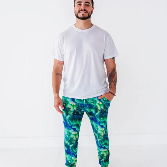 A man in a white tee wearing jogger pajama pants with a green and blue northern lights pattern with stars.