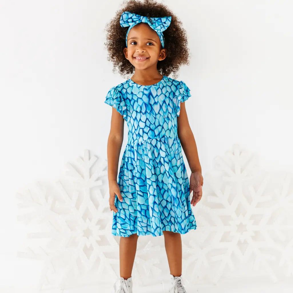 Young girl wearing a blue patterned dress and headband against a white background