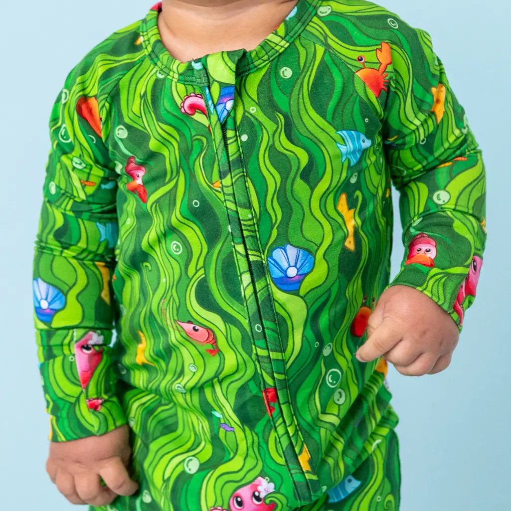 Child wearing a green patterned shirt with fish and shell design on a light blue background