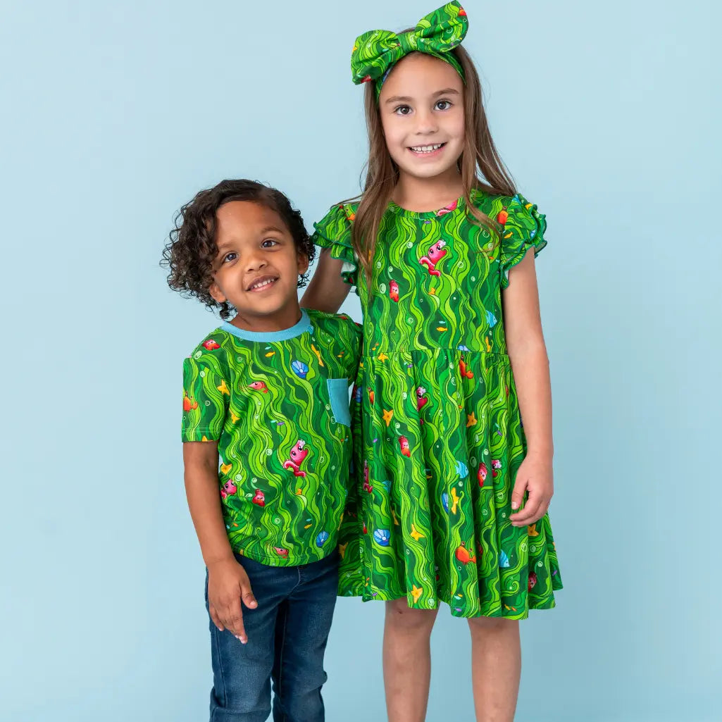Two children wearing matching green outfits with a wavy pattern on a light blue background