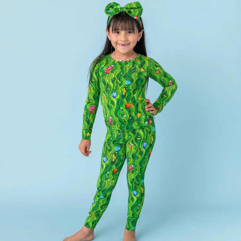 Child wearing a green patterned onesie against a light blue background