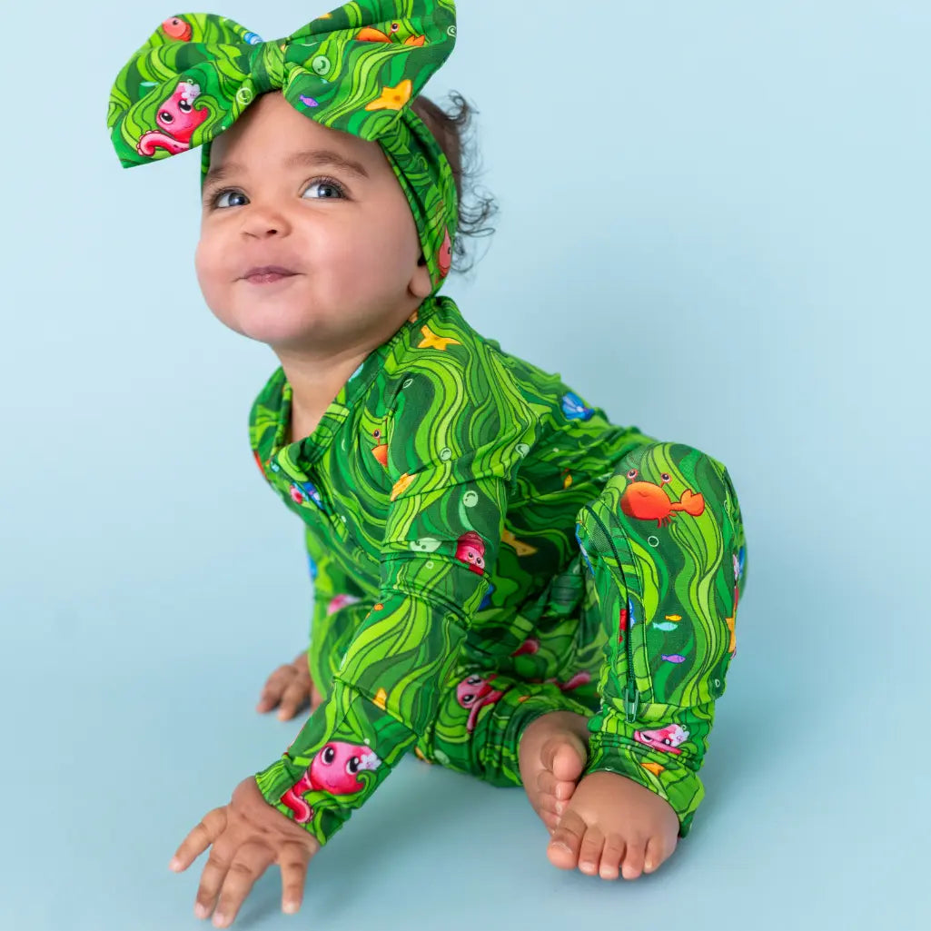 Child wearing a green patterned outfit with a matching headband on a light blue background