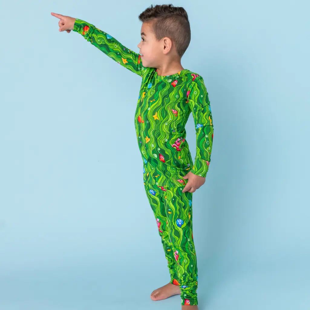 Child wearing a green patterned onesie against a light blue background