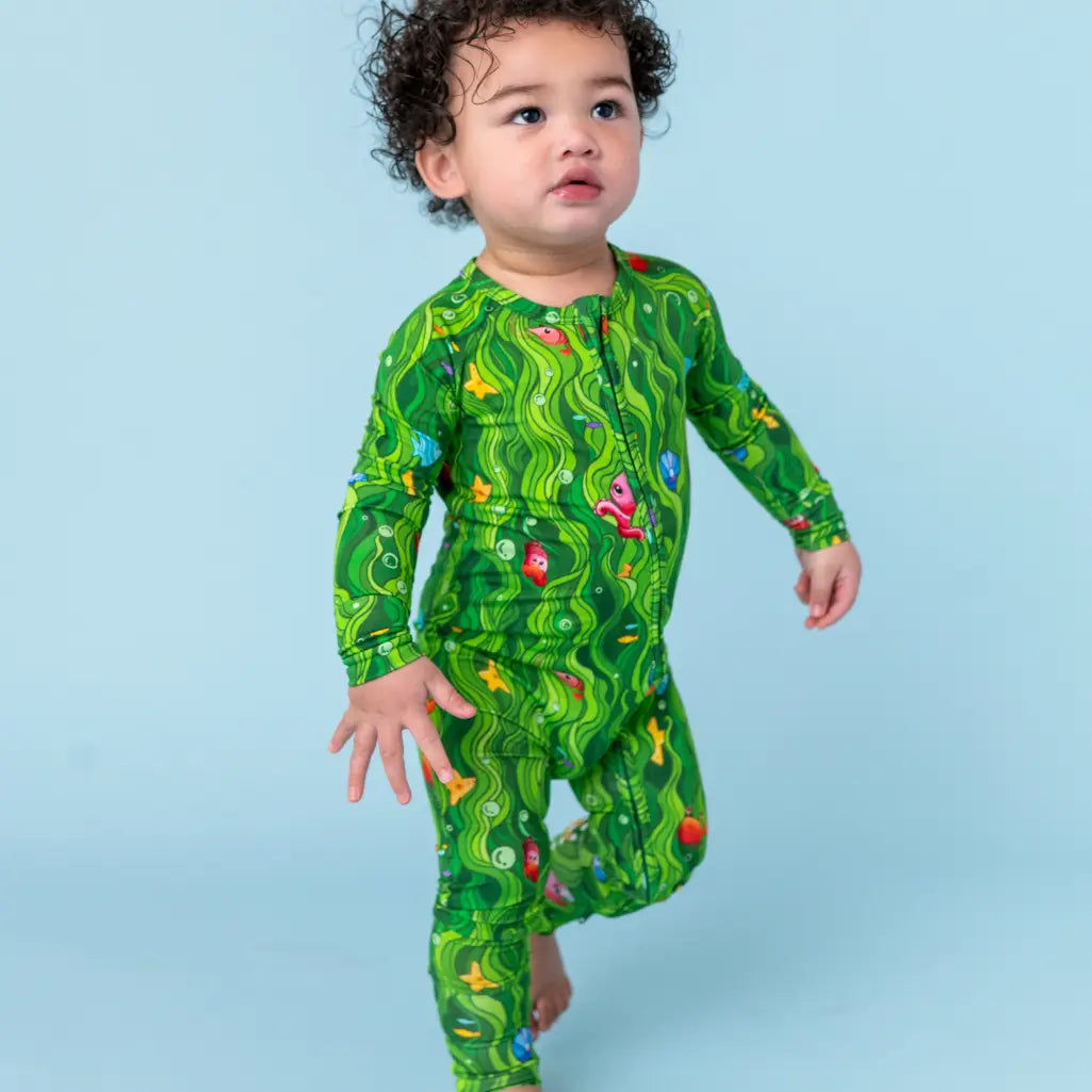 Child wearing a green patterned onesie on a light blue background