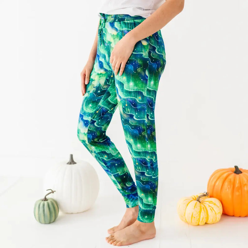 Person wearing green and blue wave-patterned leggings standing barefoot next to pumpkins on a white background.