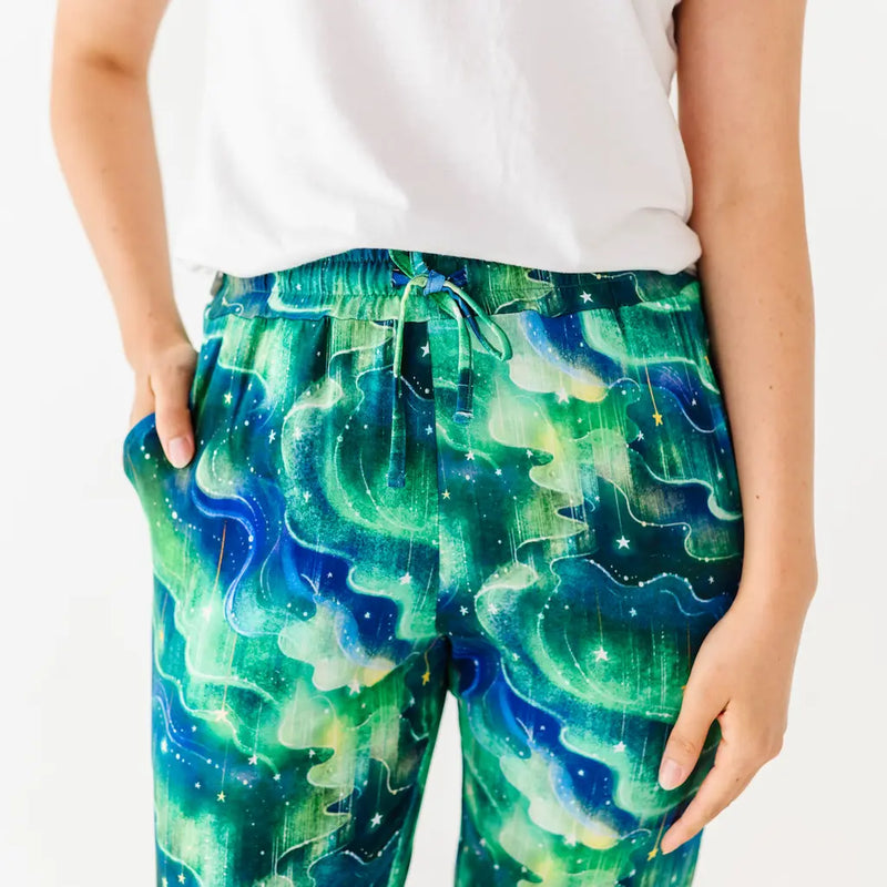 Close-up of a person wearing green and blue wave-patterned pants and a white shirt with hands in pockets against a white background.