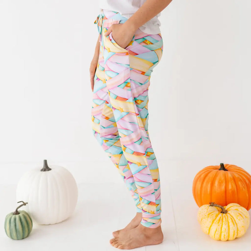 Colorful pastel candy-striped leggings worn by a person standing barefoot among pumpkins on a white background.