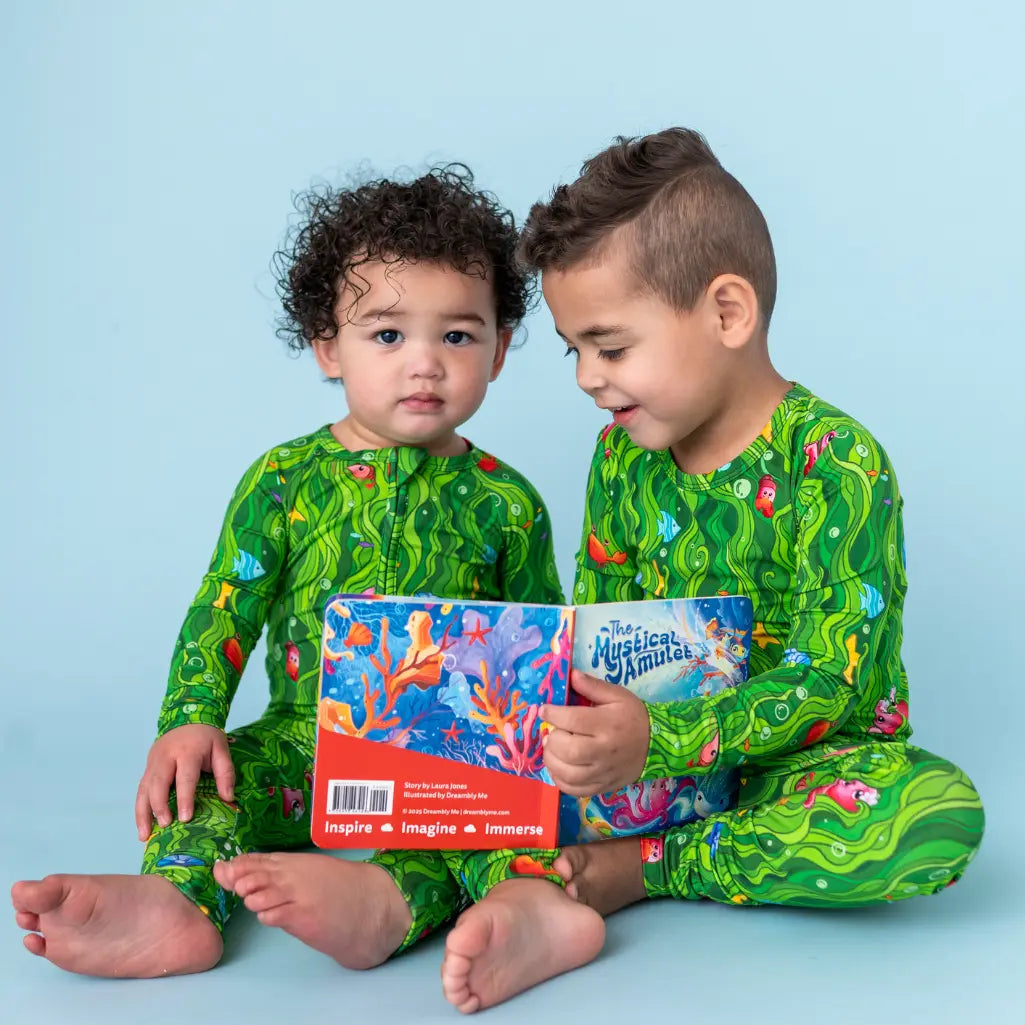 Two children in matching green pajamas with a book on a blue background