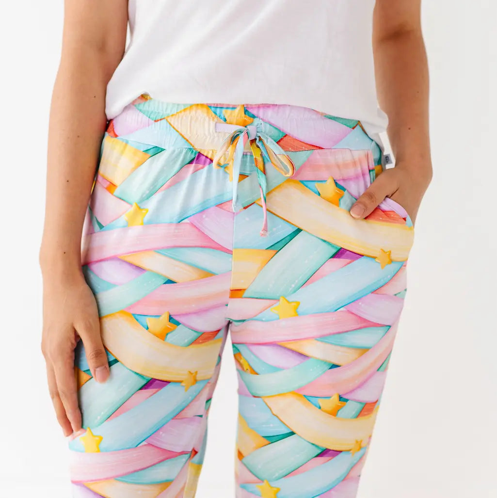 Close-up of a person wearing pastel multicolored candy ribbon pattern pants with yellow stars and a drawstring at the waist against a white background.