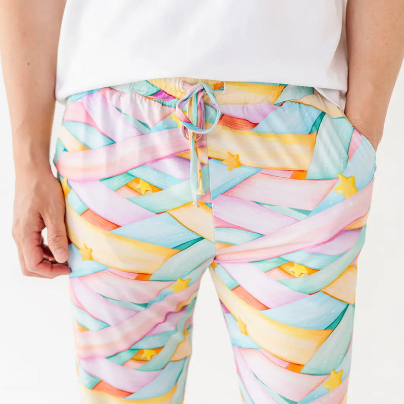 Close-up of pastel candy ribbon-patterned pants with a drawstring and yellow stars, worn by a person in a white shirt against a white background.