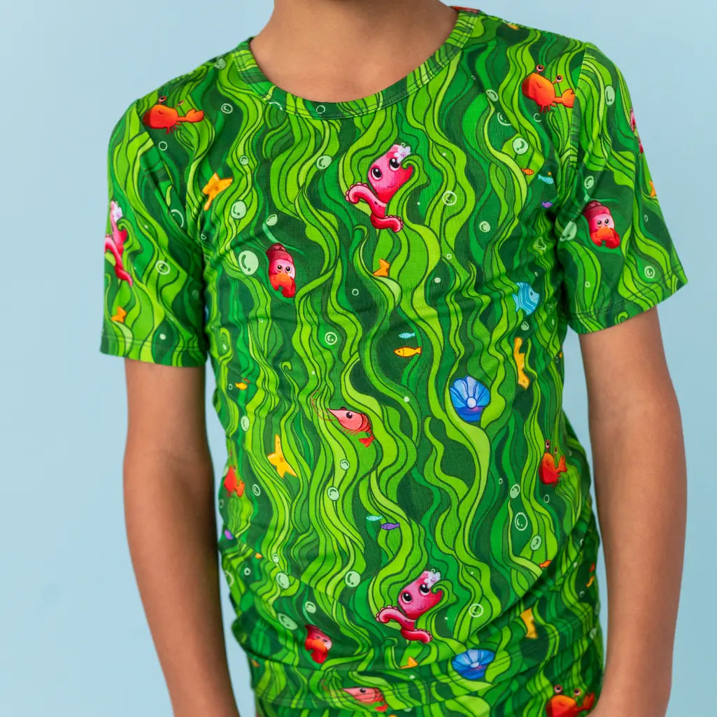 Green t-shirt with colorful fish pattern worn by a person on a light blue background