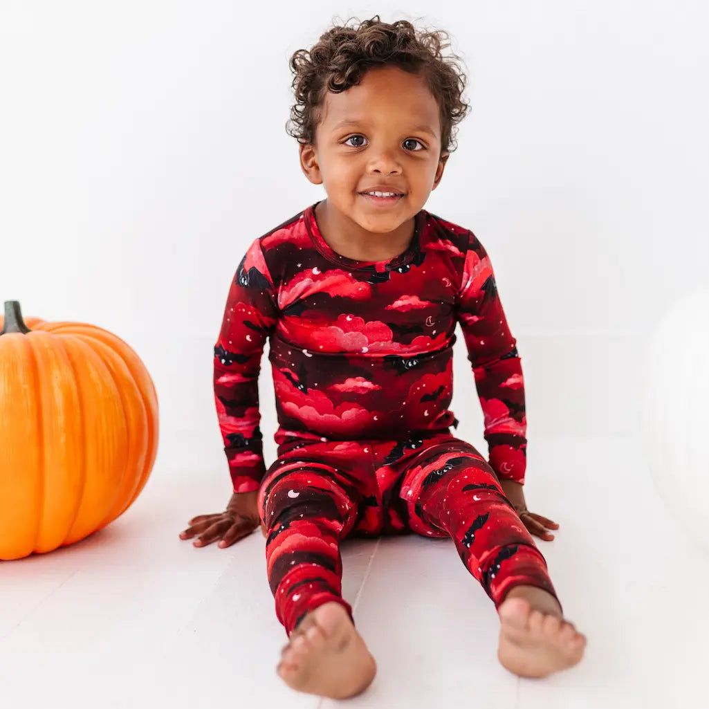 Child wearing red and black patterned pajamas sitting next to a pumpkin on a white background