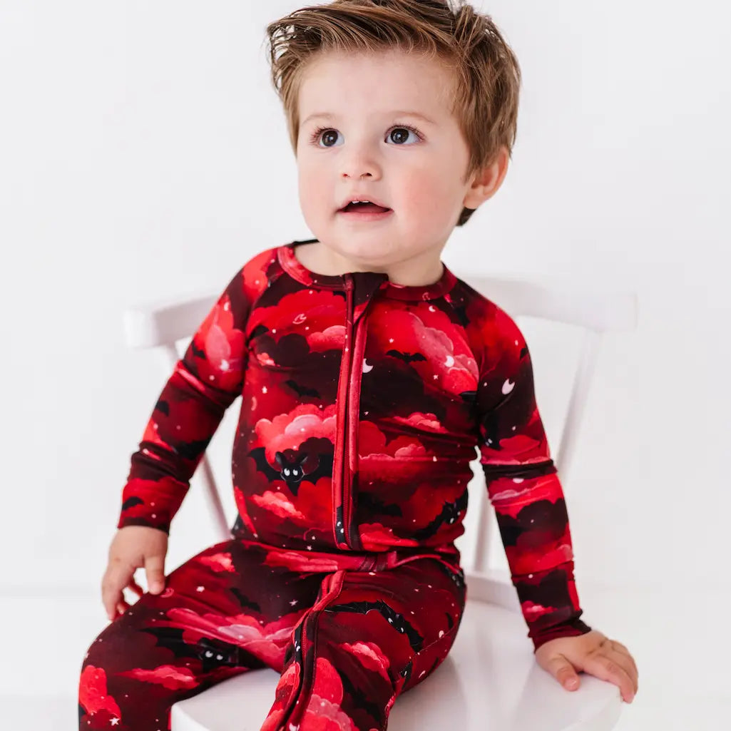 Child wearing a red and black floral patterned onesie on a white background
