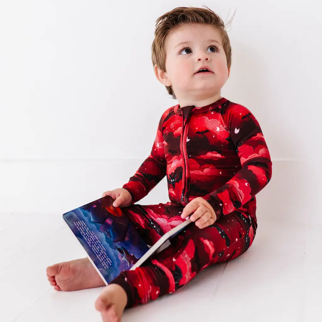 Child wearing a red and black patterned onesie holding a book on a white background