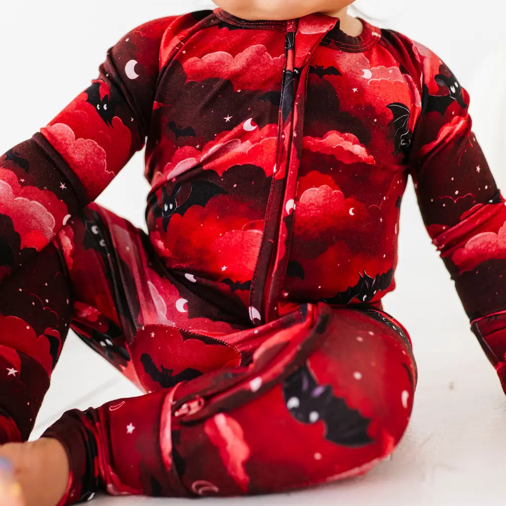 Baby in a red and black cloud-patterned onesie sitting on a white surface.