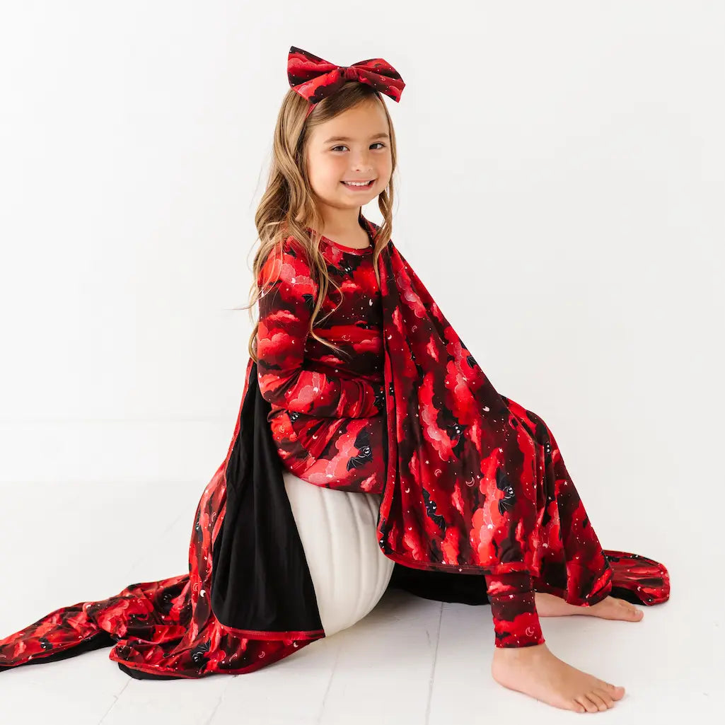 Child wearing a red and black patterned outfit with a large bow on a white background