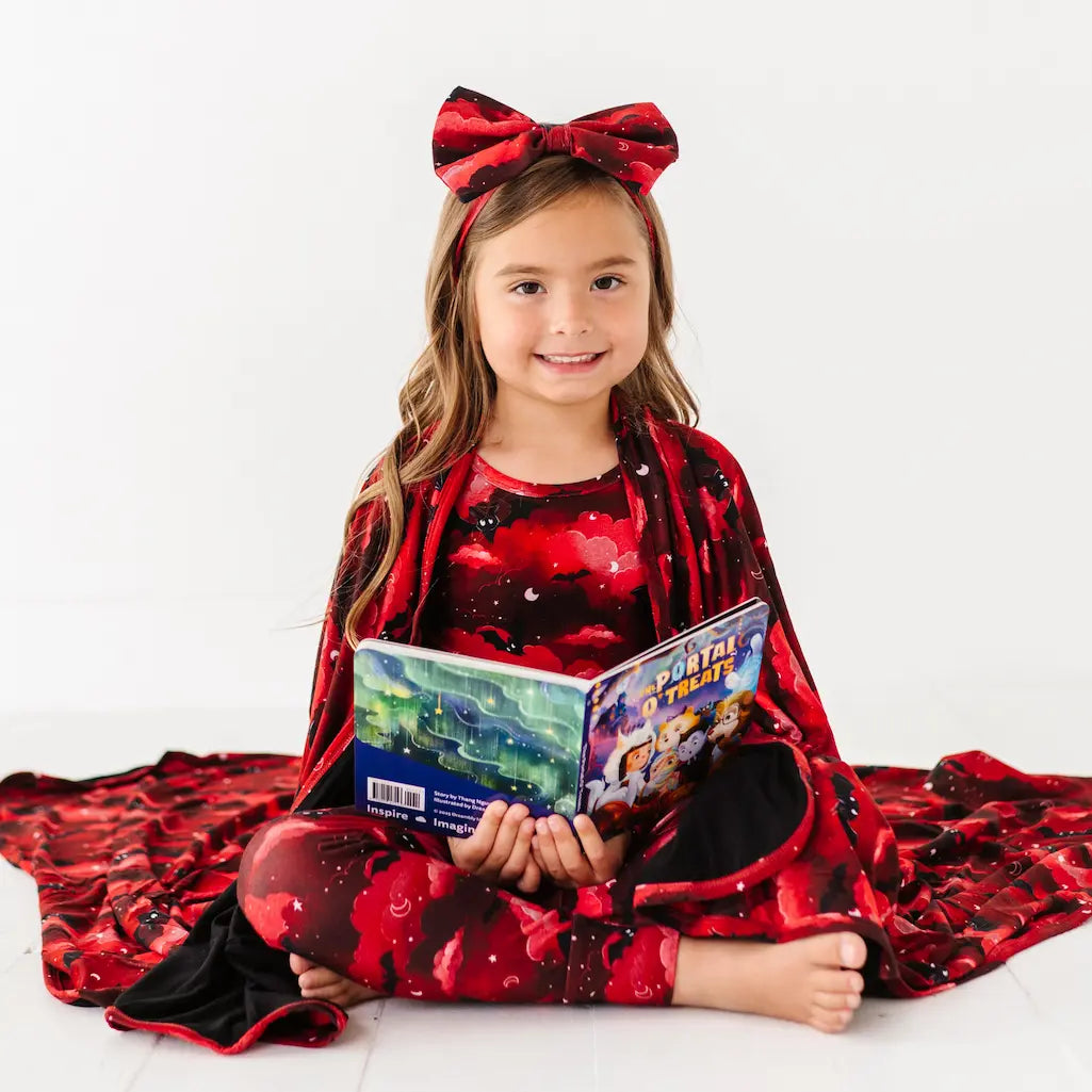 Young girl in a red and black outfit with a large bow, holding a book on a white background
