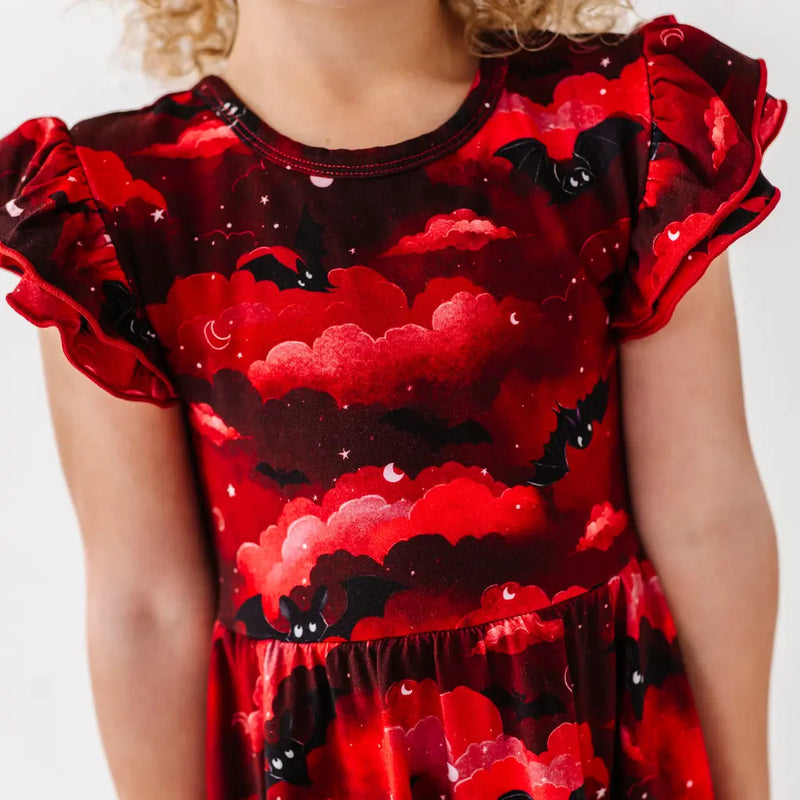 Red dress with black bat and cloud pattern worn by a child on a white background