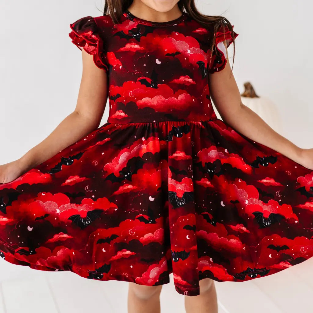 Child wearing a red dress with black bat and moon pattern on a white background