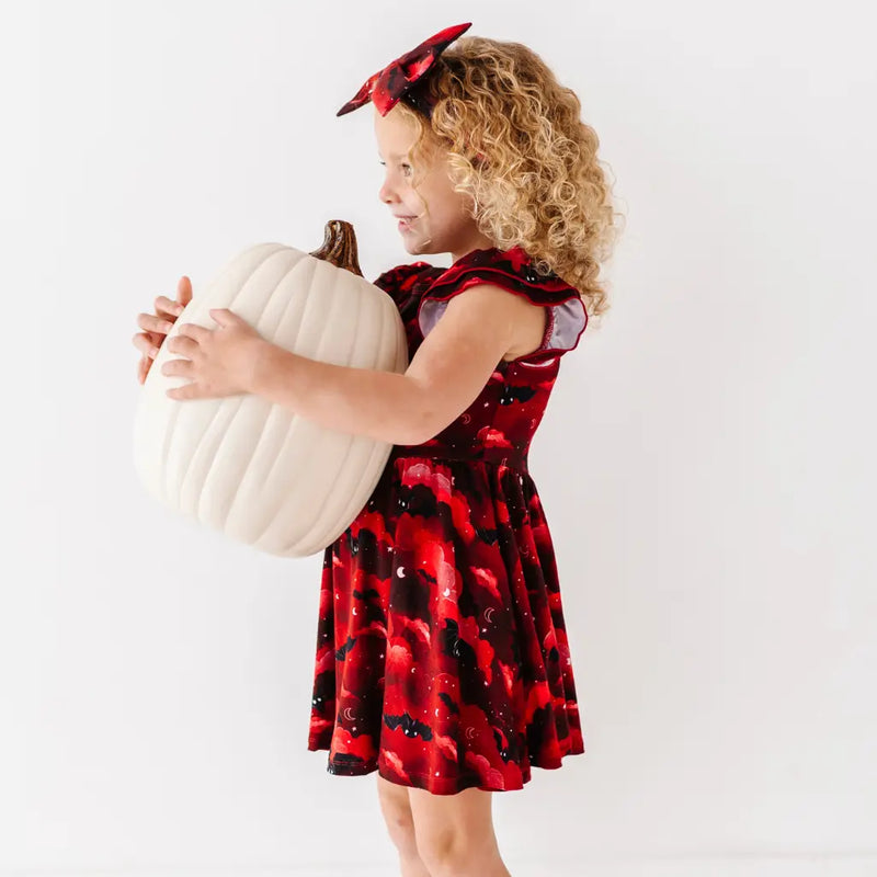 Child in a red and black dress holding a white pumpkin against a white background