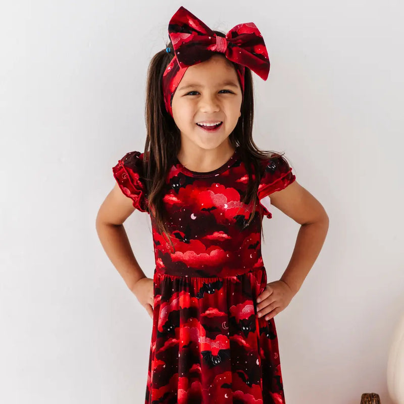 Young girl wearing a red dress with floral pattern and matching headband against a white background