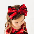 Child wearing a large red and black bow headband on a white background