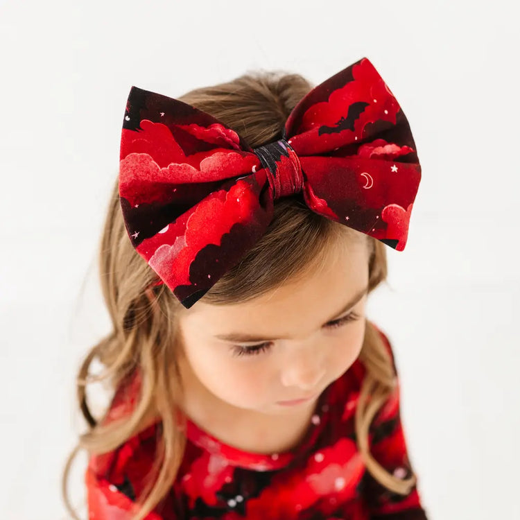 Child wearing a large red and black bow headband on a white background