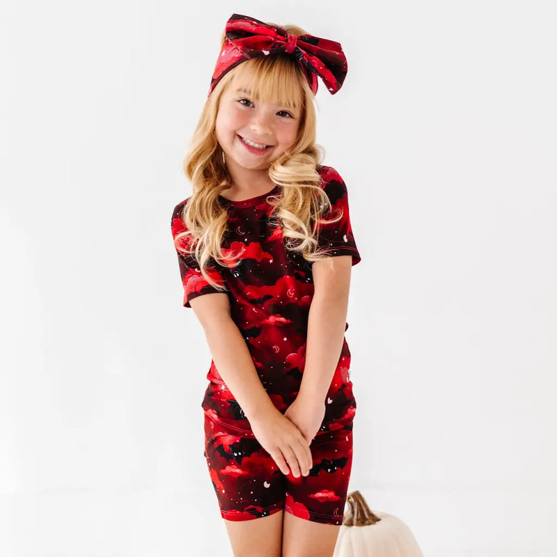 Young girl wearing a red and black floral dress with a matching headband on a white background