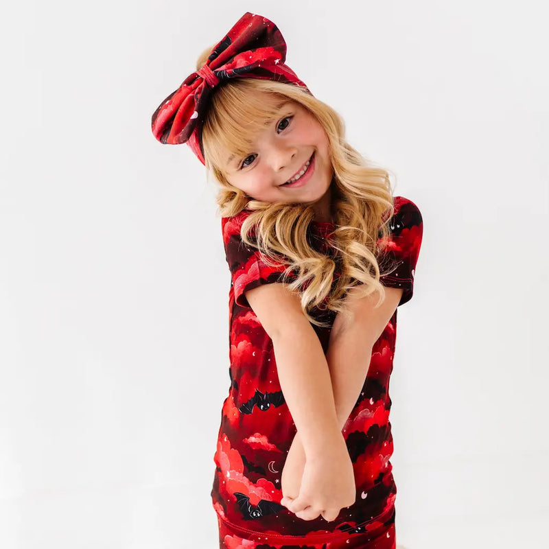 Young girl wearing a red and black floral dress with a matching headband on a white background