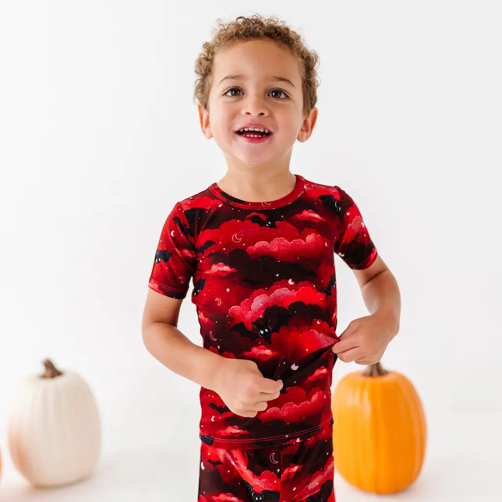 Child wearing a red and black patterned shirt with pumpkins in the background