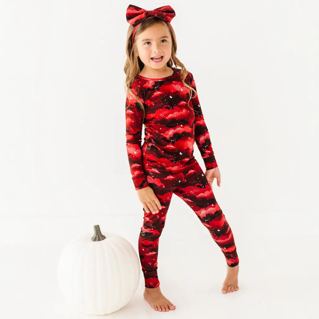 Child wearing a red and black patterned outfit with a bow, standing next to a white pumpkin on a white background.