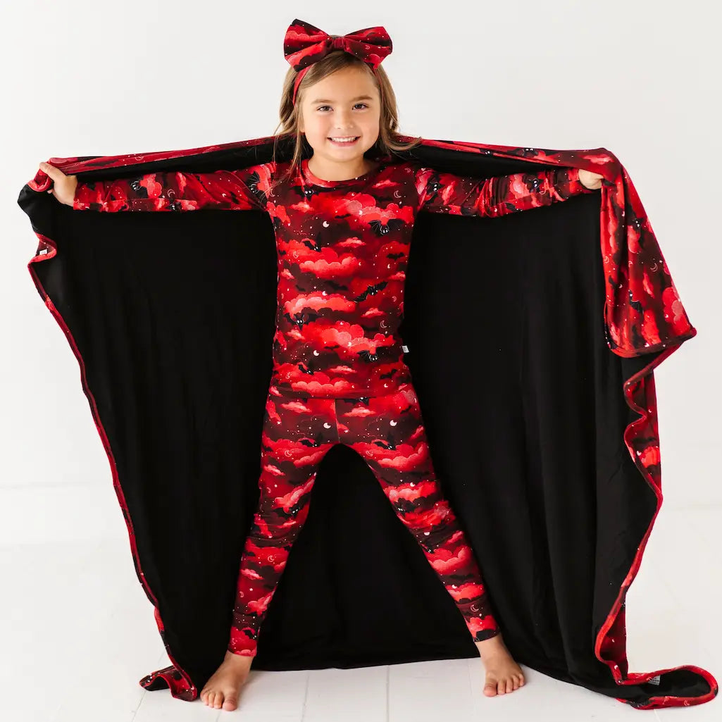 Child wearing a red and black patterned onesie with a matching cape on a white background