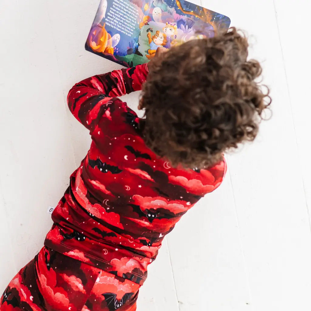 Child wearing a red and black patterned outfit with a colorful card in the background
